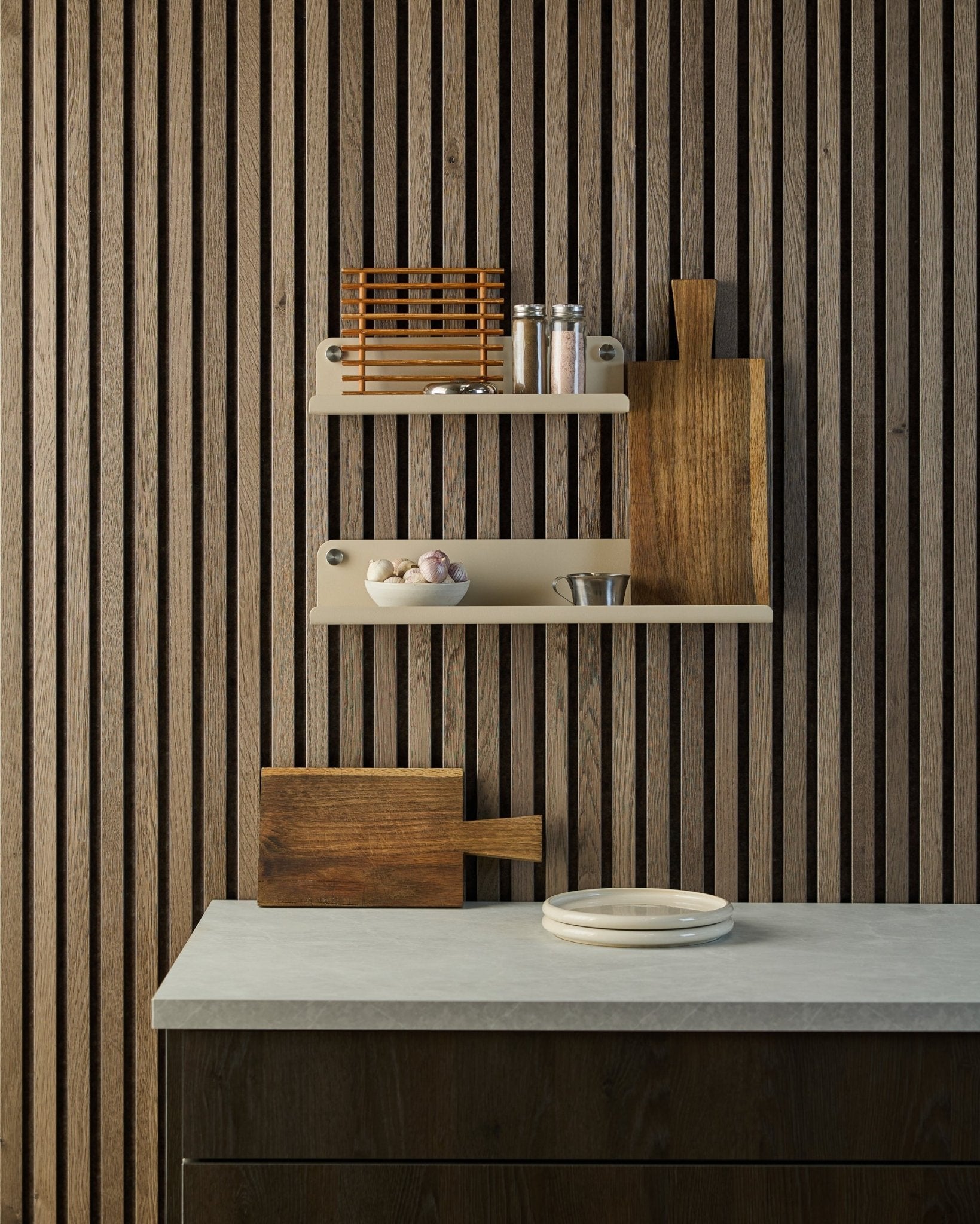 Minimalistyczna kuchnia z nordycką drewnianą ścianą akustyczną z lameli w kolorze Akupanel, otwartymi półkami na przyprawy i miski oraz blatem z białymi talerzami i deską do krojenia.